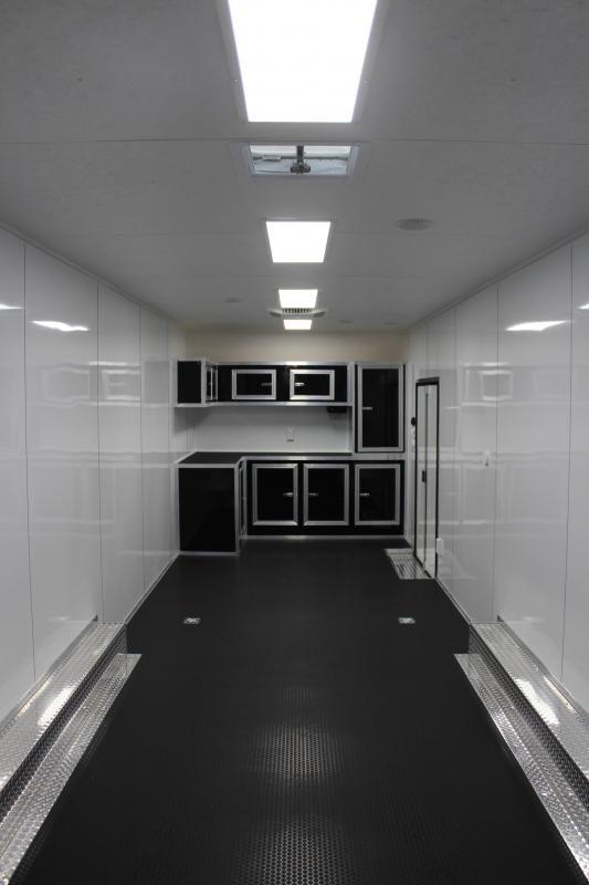 Enclosed Car Hauler 2023 30' Front Interior View. Black L-Shape Base & Overhead Cabinets, Aluminum Walls, Rubber Coin Flooring, D-Rings.