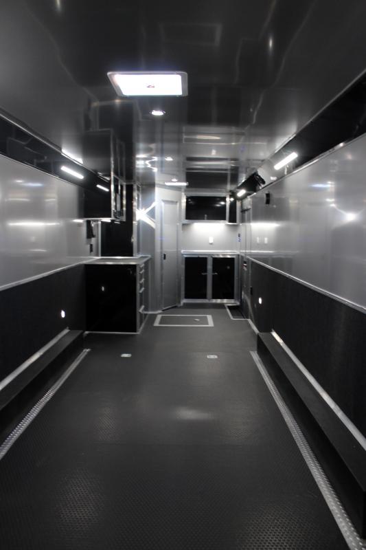 Enclosed Car Hauler 2024 34' Edge Front Interior View. It features a full black cabinet package with toolbox, coin floor, & recessed spare tire compartment.