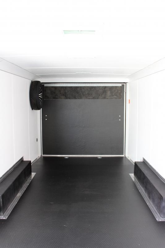 2024 24' Haulmark heat rear interior view that includes black rubber coin flooring, white vinyl walls, white cove, white vinyl ceiling, spare aluminum tire interior mounted, ramp door with flap, and d-rings.