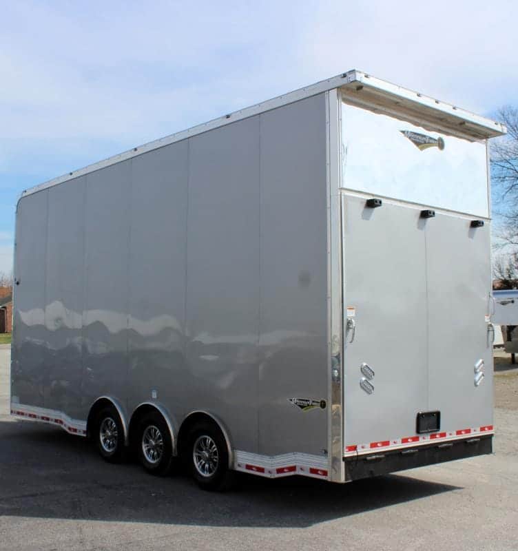 Enclosed Stacker Trailer Rear Roadside View 2024 24' Silver Eliminator. It features the rear ramp door, aluminum wheels, bonded exterior, & L.E.D. lighting.