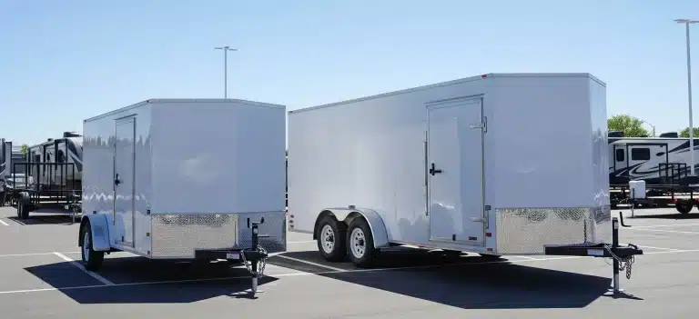 A-single-axle-and-a-double-axle-enclosed-trailer-parked-side-by-side-in-a-lot